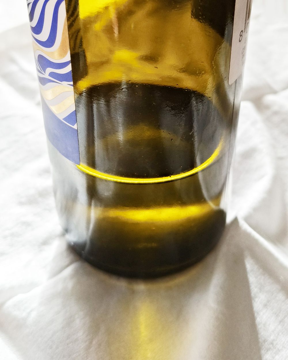 Una bottiglia di olio extra vergine di oliva in vetro scuro, attraversata dalla luce, su un panno bianco